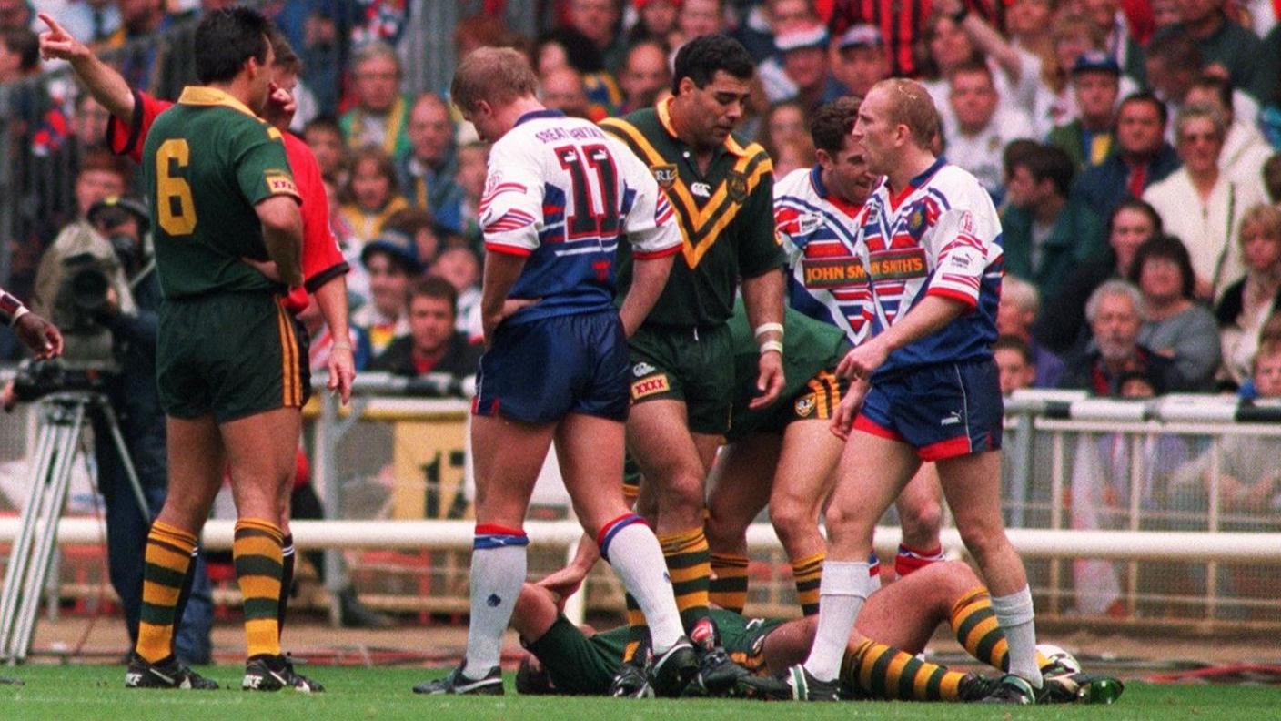 Shaun Edwards looks to the referee as a group of Australia players gather, with Bradley Clyde flat out on the ground
