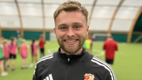 Andy Tye smiling and wearing a black Swindon Town FC Foundation top. He has short mousy-brown coloured hair and a beard.